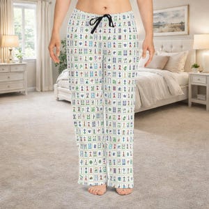 May include: White pajama pants with a black drawstring. The pants are covered in a colorful pattern of Mahjong tiles. The tiles are in shades of green, blue, red, and yellow.