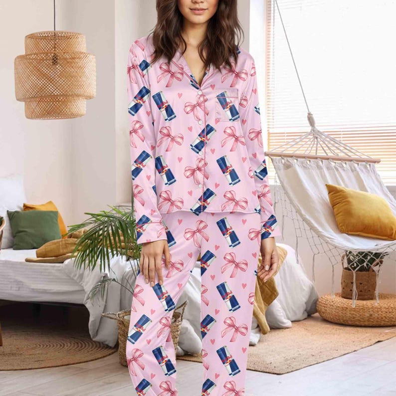Puede incluir: Conjunto de pijama de sat&eacute;n rosa con un estampado repetido de latas de bebidas azules y blancas, lazos rosas y peque&ntilde;os corazones rosas. La parte superior de manga larga tiene una parte delantera abotonada y un bolsillo en el pecho. Los pantalones tienen cintura el&aacute;stica.
