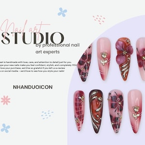 May include: A collection of artificial nails with various designs, including floral accents and jewel embellishments. The nails feature a gradient of pink and red hues, with some showcasing intricate patterns. The image also includes the text "Nail art STUDIO by professional nail art experts."