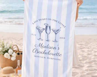 May include: A white and pale blue striped beach towel with text that reads "Last Toast on the Coast" and "Madison's Bachelorette". The towel features illustrations of cocktails.