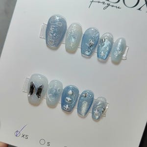 May include: Two sets of light blue press-on nails with various designs, including glitter, stars, and a butterfly. The top of the card reads "NAIL BOX for you". Sizes XS, S, M, and L are indicated.