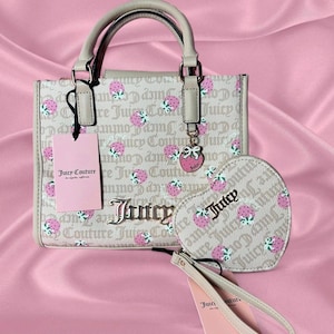 May include: A beige Juicy Couture handbag and heart-shaped purse, both patterned with pink strawberries and the Juicy Couture logo. The handbag has a top handle and a strawberry charm. A pink tag is attached to the handbag.