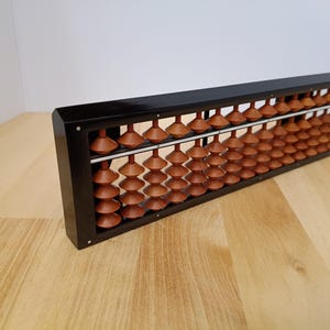 May include: A traditional abacus featuring a rectangular black frame and multiple columns of polished brown wooden beads. The beads are shaped like double cones and are arranged on thin metal rods, separated by a horizontal divider bar.