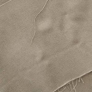 Op de afbeelding: Close-up van verschillende stukken beige stof met een getextureerde, geribbelde weefsel. De randen zijn onafgewerkt, met losse draden zichtbaar. De stof lijkt een materiaal van gemiddeld gewicht te zijn, mogelijk voor kleding of woondecoratie.