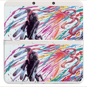 May include: A white handheld gaming console featuring a graphic of a dark, chainsaw-wielding character with a long red scarf. The design includes vibrant, multi-colored paint splatters in pink, blue, yellow, and green across the entire surface.
