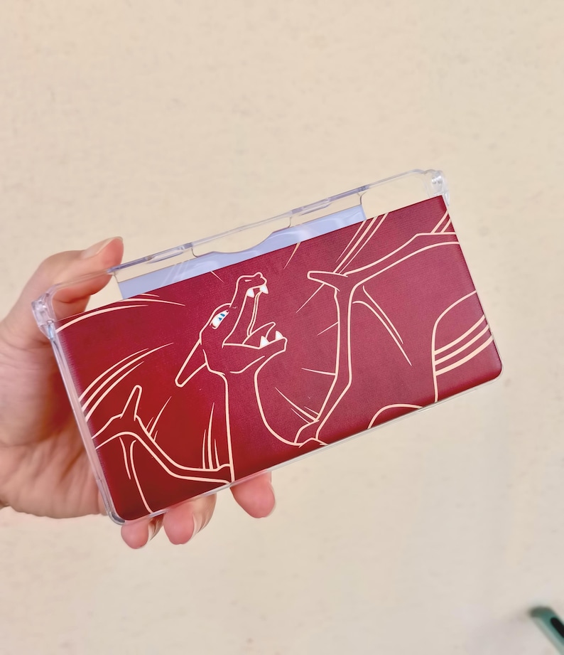 May include: A clear plastic case with a burgundy background featuring a white line drawing of a dragon. The dragon is depicted with its mouth open, and the case is designed to fit a handheld gaming device.