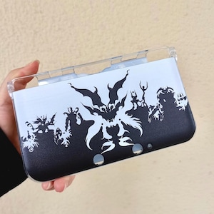 May include: A black and white Nintendo 3DS case with a clear plastic top. The case features a graphic silhouette design, possibly from a fantasy or gaming theme. The design is predominantly black and white.