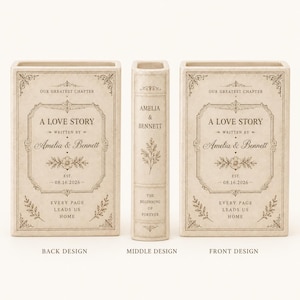 May include: A cream-colored ceramic book-shaped vase featuring black text and floral illustrations. The front and back display 'A LOVE STORY', 'Amelia & Bennett', and '08.16.2026'. The spine reads 'AMELIA & BENNETT' and 'THE BEGINNING OF FOREVER'.