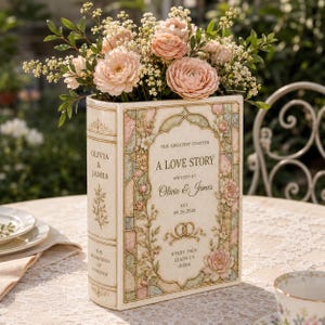 May include: A rectangular book-shaped vase in cream with pastel floral accents and stained glass patterns. The text reads: Our Greatest Chapter, A Love Story, Written By Olivia & James, Est. 09.26.2026, The Beginning Of Forever, Every Page Leads Us Home.