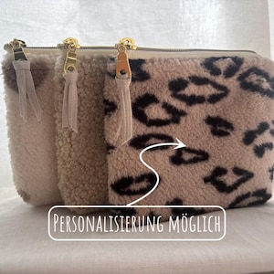 Puede incluir: Tres neceseres con cremallera y peludos en crema, beige y estampado de leopardo. Cada neceser tiene una cremallera dorada y una borla a juego. El neceser con estampado de leopardo tiene manchas negras. El texto en la imagen dice "PERSONALISIERUNG MÖGLICH".