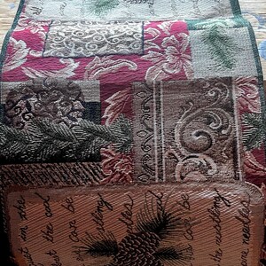 Puede incluir: Un tapiz rectangular con un diseño de patchwork. El tapiz presenta varios patrones, incluyendo motivos florales y de piñas, en tonos de rojo, verde y marrón. La sección inferior tiene texto y una ilustración de piña.