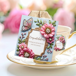 May include: A light blue greeting card with a gold frame and the word "Congratulations". The card is decorated with pink flowers and a butterfly. The card is next to a teacup and saucer.