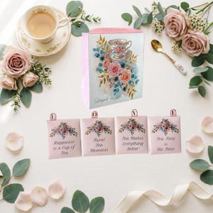 Puede incluir: Un arreglo temático de té con una taza, rosas y bolsitas de té. Las bolsitas de té tienen diseños florales y textos como "Happiness is a Cup of Tea", "Floral Tea Moments", "Tea Makes Everything Better" y "Tea Time is Me Time".