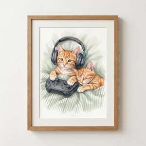 Könnte beinhalten: Aquarelldruck von zwei orangefarbenen Tabby-Kätzchen. Eines der Kätzchen trägt Kopfhörer und hält einen schwarzen Gamecontroller. Das andere Kätzchen schläft. Der Druck ist in einem hellbraunen Holzrahmen gerahmt.
