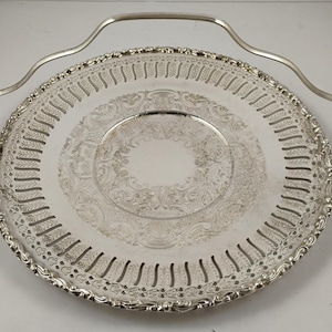 May include: Silver-plated serving tray with a decorative floral pattern and a handle. The tray has a pierced design around the edge and a detailed central medallion. The handle is curved and attached to the tray's rim.