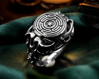 May include: A silver ring featuring a circular top with an engraved labyrinth pattern and a central star symbol. The band has a complex, organic, and textured design with deep grooves and polished metallic surfaces throughout the entire piece.