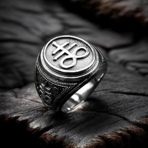 May include: A silver ring with an ornate design. The ring showcases a central symbol, encircled by detailed patterns. The ring is set against a dark, textured backdrop, emphasising its metallic shine and craftsmanship.