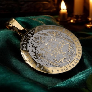 May include: A circular gold-toned pendant featuring a central white inlay with intricate black line art depicting geometric sigils, flames, and pillars. The outer gold rim is engraved with a series of small symbols and crosses around the edge.