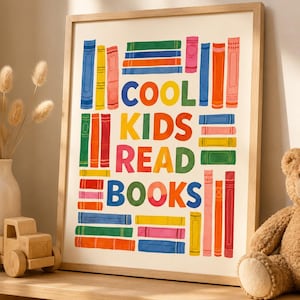 May include: A framed print with the words "COOL KIDS READ BOOKS" in colorful letters. The artwork features illustrations of books in various colors, including blue, yellow, pink, and orange. The frame is made of light-colored wood, and the print is displayed on a shelf.