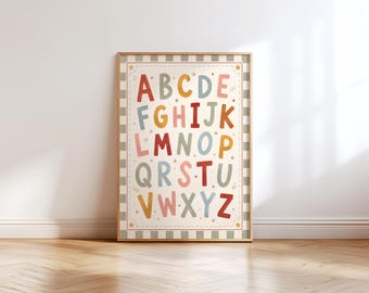 May include: A framed alphabet poster with colorful letters and star accents. The letters are in various colors, including red, blue, yellow, and pink, set against a cream background with a striped border. The poster is displayed on a wooden floor.