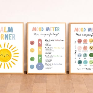 Könnte beinhalten: Drei gerahmte Drucke mit Holzrahmen. Der linke Druck zeigt "CALM CORNER" mit einer lächelnden Sonnenillustration. Die anderen beiden Drucke tragen den Titel "MOOD METER" mit einer Skala von Emotionen und Maßnahmen.