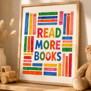 May include: A framed print with the text "READ MORE BOOKS" in vibrant colours. The artwork showcases illustrated books in shades of blue, green, orange, and pink, arranged around the text. The frame is made of light-coloured wood, suitable for a child's room.