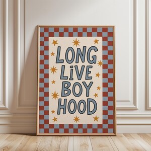 May include: Framed art print with the words "LONG LIVE BOY HOOD" in blue lettering on a cream background, surrounded by gold stars. The frame has a red and blue checkered border.