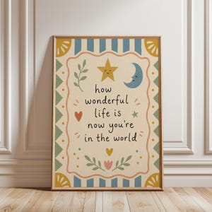 May include: A framed art print with the words "how wonderful life is now you're in the world." The print features a yellow star and moon, a red heart, and floral accents. The border has blue stripes and yellow and green decorative elements.