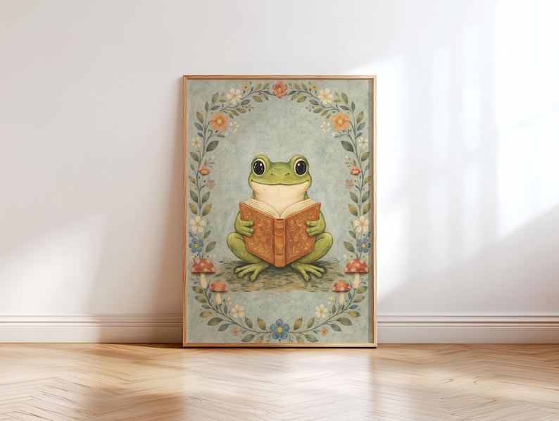 May include: A framed art print featuring a whimsical illustration of a green frog reading a book. The frog is surrounded by a floral wreath with mushrooms at the base. The artwork has a vintage, storybook aesthetic, with soft colors and a light blue background.