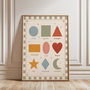 May include: A framed educational poster featuring various colorful geometric shapes, including a circle, square, triangle, rectangle, oval, heart, star, diamond, and crescent. Each shape is labeled with its name in a playful font, with star accents.