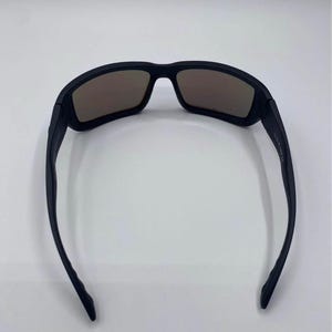 May include: Black sunglasses with brown tinted lenses. The sunglasses have a rectangular frame and a sleek, modern design. The arms of the sunglasses are thin and curve slightly.