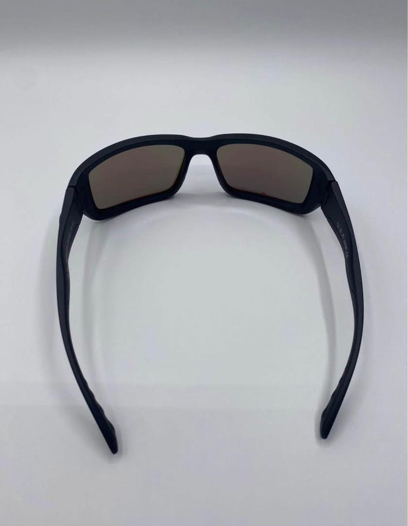 May include: Black sunglasses with brown tinted lenses. The sunglasses have a rectangular frame and a sleek, modern design. The arms of the sunglasses are thin and curve slightly.
