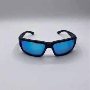 May include: Black sunglasses with blue mirrored lenses. The sunglasses have a rectangular frame and curved temples. The lenses reflect a bright blue color, and the frame appears to be made of a matte black material.