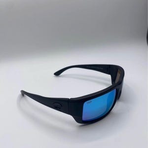 May include: Black sunglasses with blue mirrored lenses. The sunglasses have a thick, rectangular frame and curved temples. The lenses are marked with "580P". The sunglasses are designed for outdoor activities.