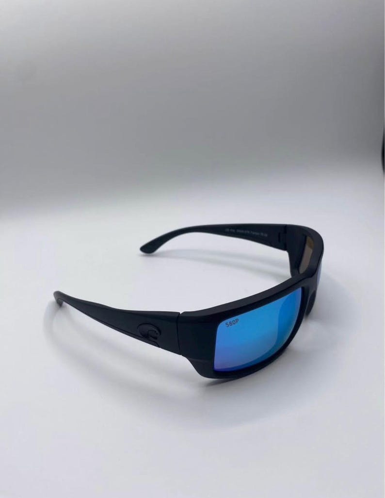 May include: Black sunglasses with blue mirrored lenses. The sunglasses have a thick, rectangular frame and curved temples. The lenses are marked with "580P". The sunglasses are designed for outdoor activities.