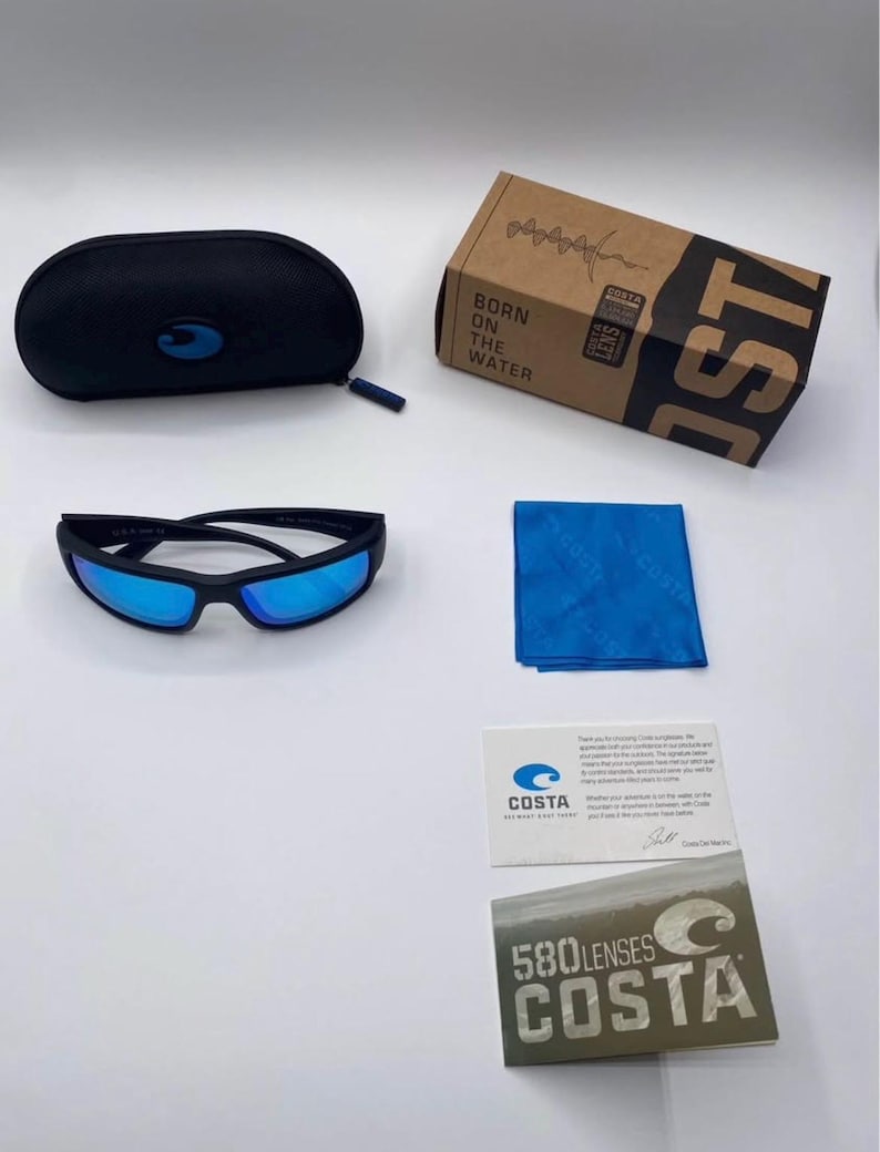 May include: Black sunglasses with blue lenses, a black case, a blue cleaning cloth, and a cardboard box with the text "BORN ON THE WATER" and "COSTA". Also included are two cards with the "COSTA" logo and text.