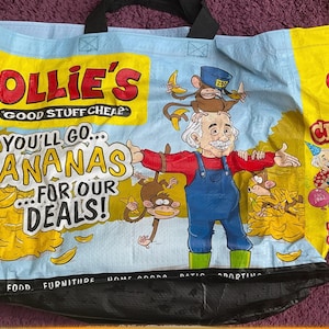 May include: Large shopping bag with a colorful design featuring a cartoon man, monkeys, and bananas. The bag has the text "Ollie's Good Stuff Cheap" and "You'll go bananas for our deals!" The bag is blue, yellow, and black.
