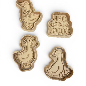 May include: Four beige plastic cookie cutters in the shape of ducks. One duck has a bow, another wears a hat, and a third is sitting. The fourth cutter has the text "One Silly Goose".
