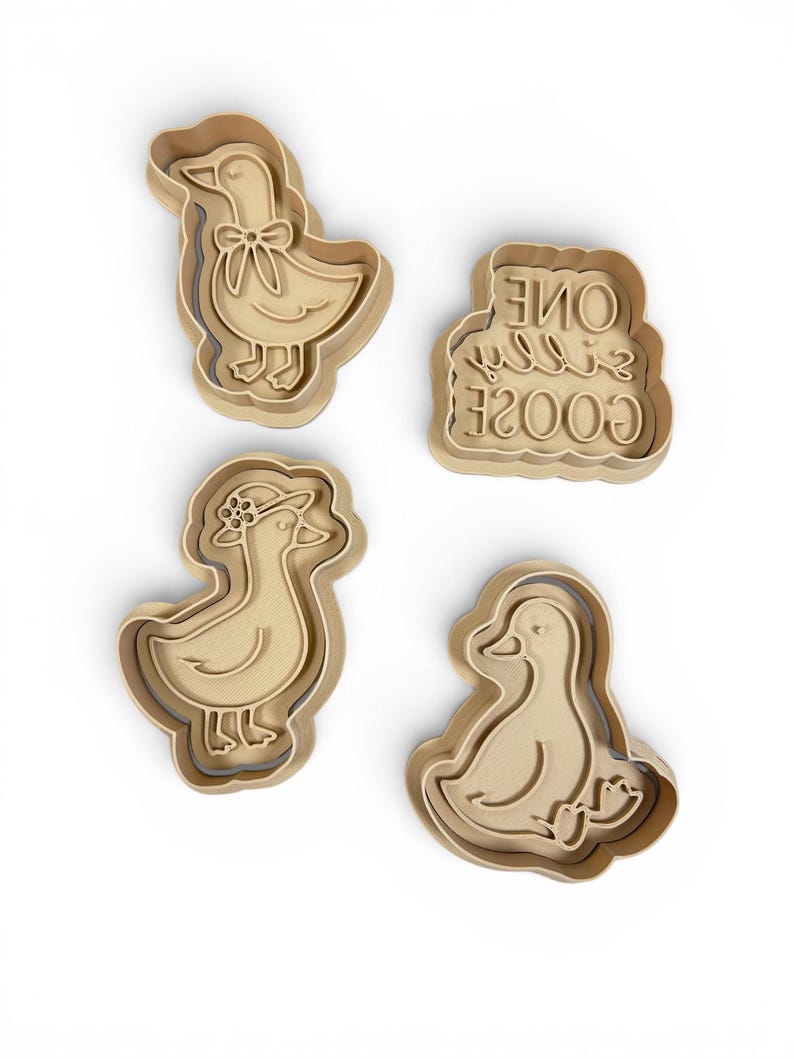 May include: Four beige plastic cookie cutters in the shape of ducks. One duck has a bow, another wears a hat, and a third is sitting. The fourth cutter has the text "One Silly Goose".