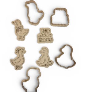 May include: A collection of light brown cookie cutters in various duck shapes, including a duck with a bow, a duck wearing a hat, and a duck sitting down. Also included is a cookie cutter with the text "ONE SILLY GOOSE".