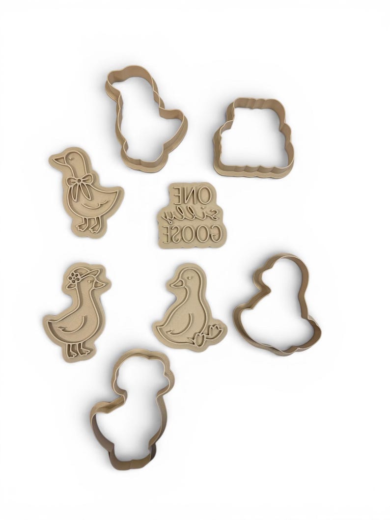 May include: A collection of light brown cookie cutters in various duck shapes, including a duck with a bow, a duck wearing a hat, and a duck sitting down. Also included is a cookie cutter with the text "ONE SILLY GOOSE".