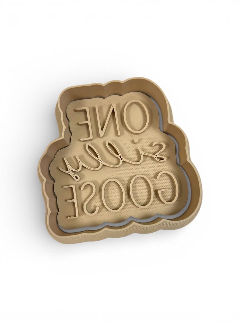 May include: A tan-colored cookie cutter in the shape of a cloud. The words "ONE" and "GOOSE" are written in a cursive font, and the numbers "2003" are written in a block font.
