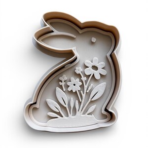May include: A white, bunny-shaped cookie cutter with a floral design. The cutter features a detailed outline of a rabbit with flowers and leaves inside. The design is raised, creating a 3D effect. Ideal for Easter or spring-themed baking.