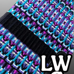 Könnte beinhalten: Ein farbenfrohes Sattelpad mit einem geometrischen Muster in Lila, Türkis und Weiß auf schwarzem Hintergrund. Die Buchstaben "LWC" sind in Weiß zu sehen. Dieses Pad ist für den Reitsport konzipiert.