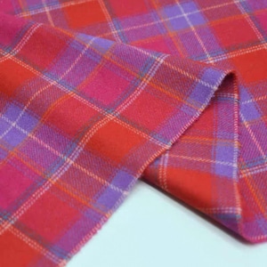 May include: A close-up shot of a colourful plaid fabric, predominantly red, pink, and purple. The tartan pattern is formed by intersecting lines, creating a grid. The fabric is folded, revealing its texture and the interplay of colours.