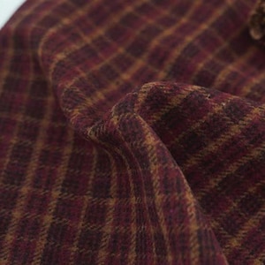 May include: Close-up of a burgundy and gold plaid fabric. The fabric has a textured appearance with a woven pattern of intersecting lines, creating a grid-like design. The colours are rich and warm, suggesting a cosy or autumnal theme.