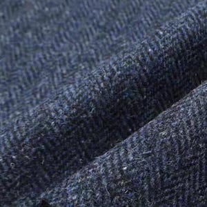 May include: Detailed shot of a navy blue herringbone fabric. The material has a textured surface with a visible weave, showing a pattern of diagonal lines. The fabric's colour varies slightly, creating depth and visual interest.