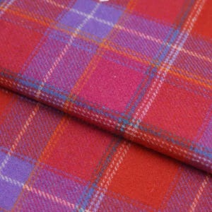 Peut inclure: Gros plan sur un tissu à carreaux vibrant dans les tons de rouge, rose et violet. Le motif présente des lignes entrecroisées créant un motif à carreaux classique. Le tissu a un aspect doux et texturé.