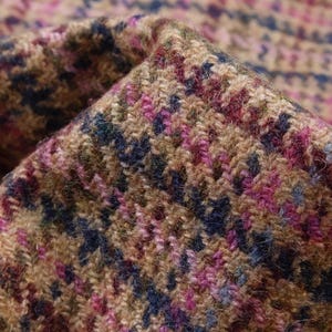 May include: Close-up of a folded fabric with a houndstooth pattern. The fabric features a mix of colors, including brown, pink, blue, and green. The texture appears to be woven, with a slightly rough surface.