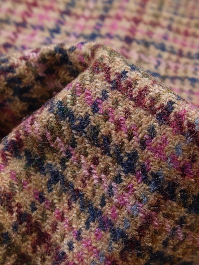 May include: Close-up of a folded fabric with a houndstooth pattern. The fabric features a mix of colors, including brown, pink, blue, and green. The texture appears to be woven, with a slightly rough surface.
